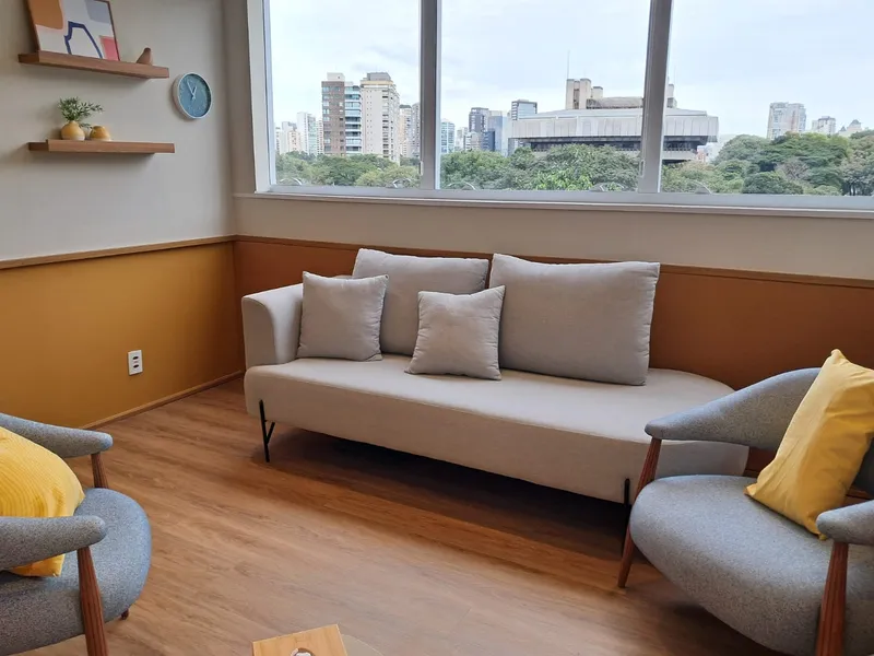 Consultório acolhedor com sofá, poltronas e uma ampla janela